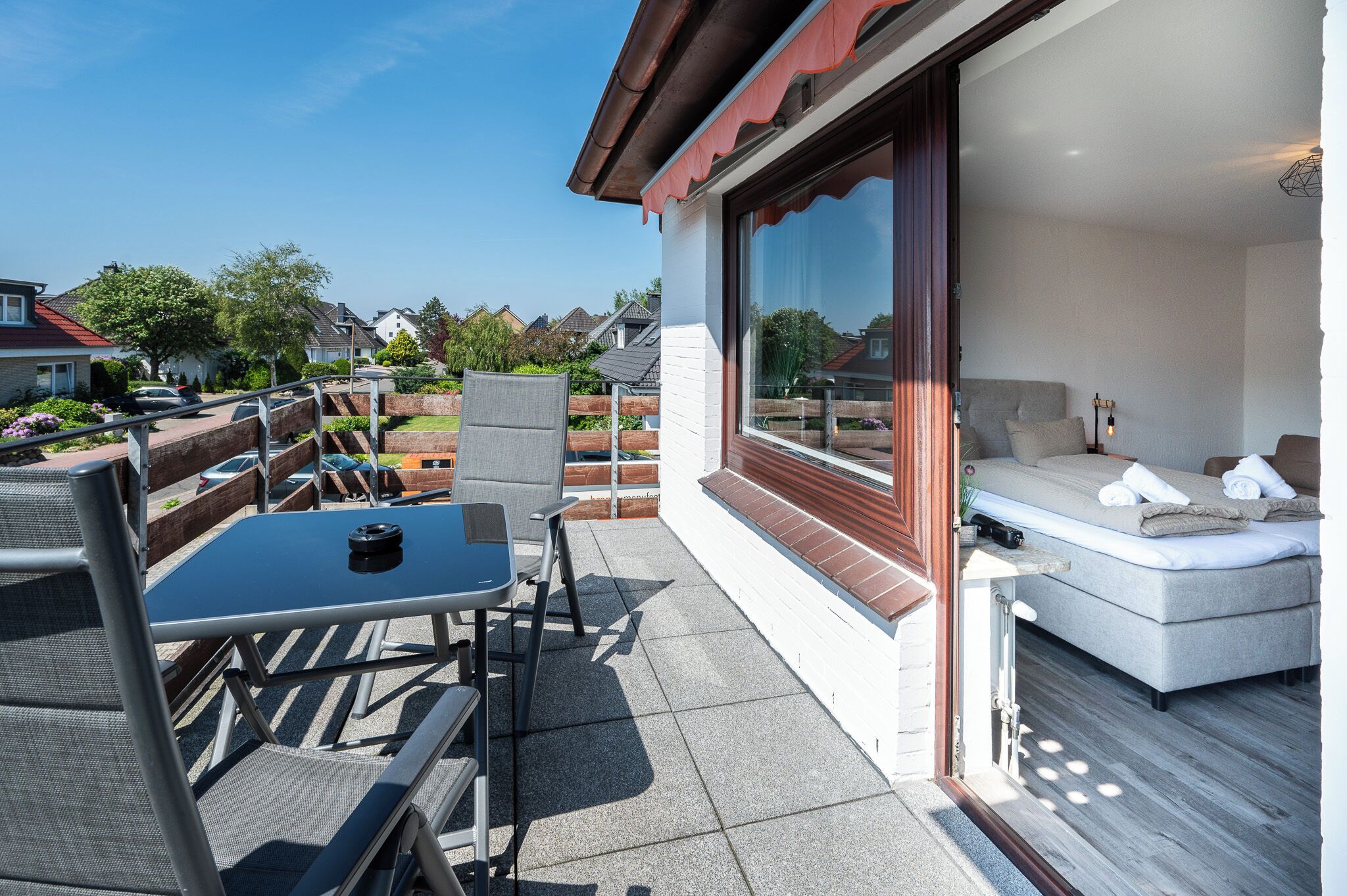 A modern outdoor patio with a dining table and chairs, a sofa, and a large sliding glass door leading to a bedroom.