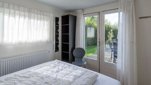 A bedroom with a bed, a radiator, a wardrobe, a chair, and a view of the outside.