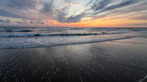 A beach with waves and a sunset.