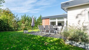 A modern building with a patio area featuring a table and chairs, surrounded by a well-maintained lawn and garden.