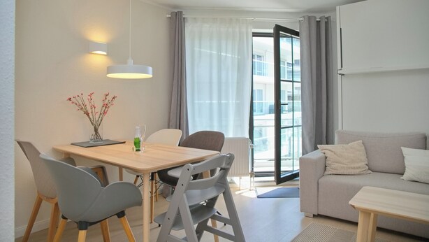 Ein modernes Wohnzimmer mit einer Couch, einem Esstisch mit Stühlen, einer Pendelleuchte und Blick durch eine Glastür.