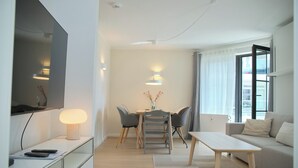 Ein modernes Wohnzimmer mit Flachbildfernseher, Esstisch mit Stühlen, einer Couch und einem Couchtisch.