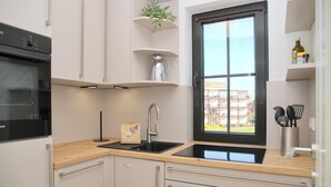 Eine moderne Küche mit einem schwarzen Spülbecken, Edelstahlgeräten und einem Fenster mit Blick auf Gebäude.