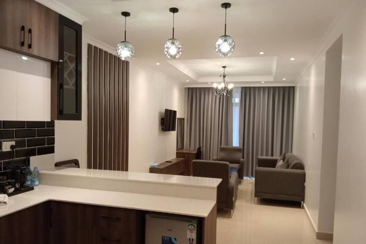 A modern kitchen with a built-in refrigerator, a dining area with a sofa, and a living room with a TV.