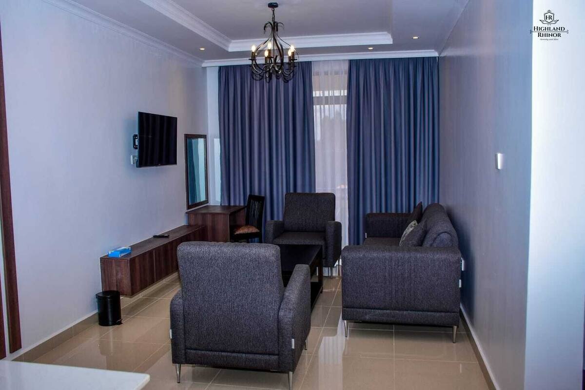 A modern living room with a chandelier, two grey sofas, a TV, and a large window with blue curtains.