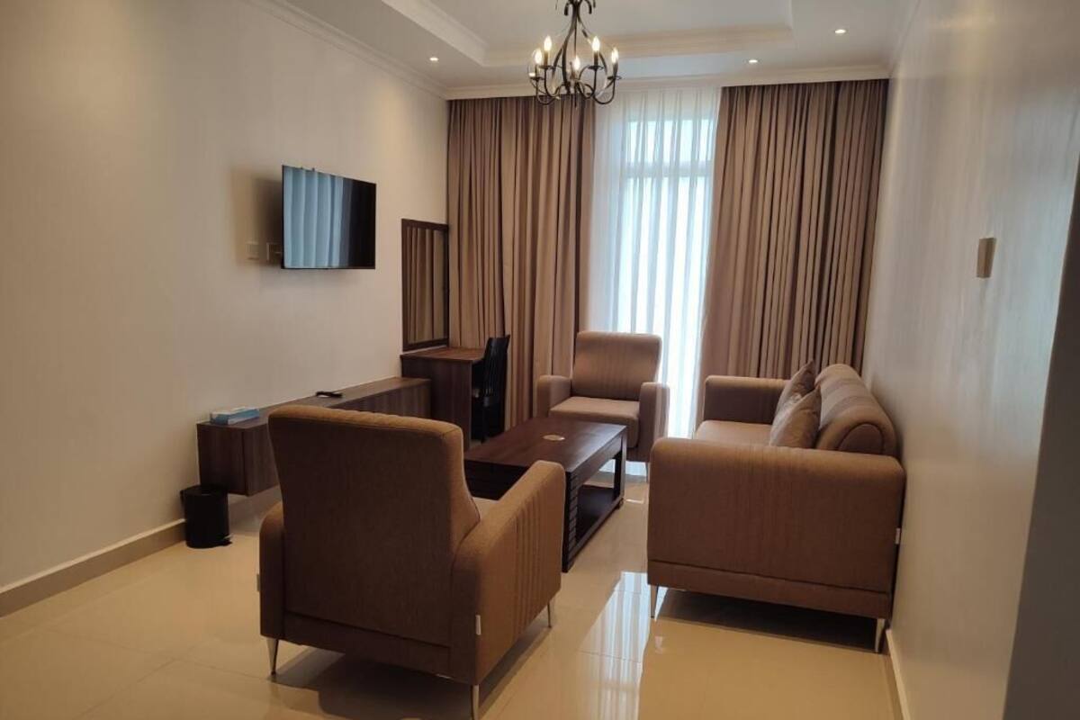 A modern living room with a sofa set, a coffee table, a TV mounted on the wall, and a chandelier.