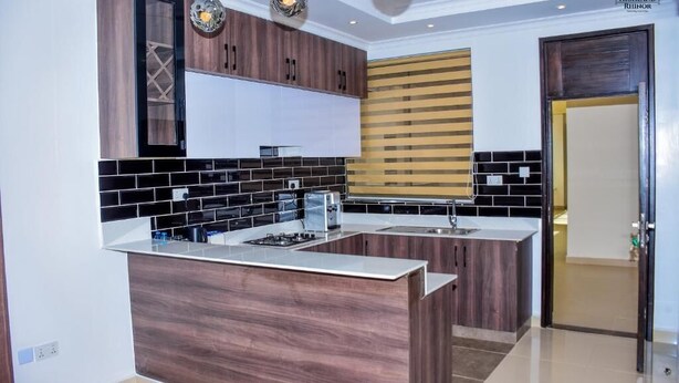 A modern kitchen with dark wood cabinets, a black and white tiled backsplash, and a central island. - Highland Rhinor (Eldoret)