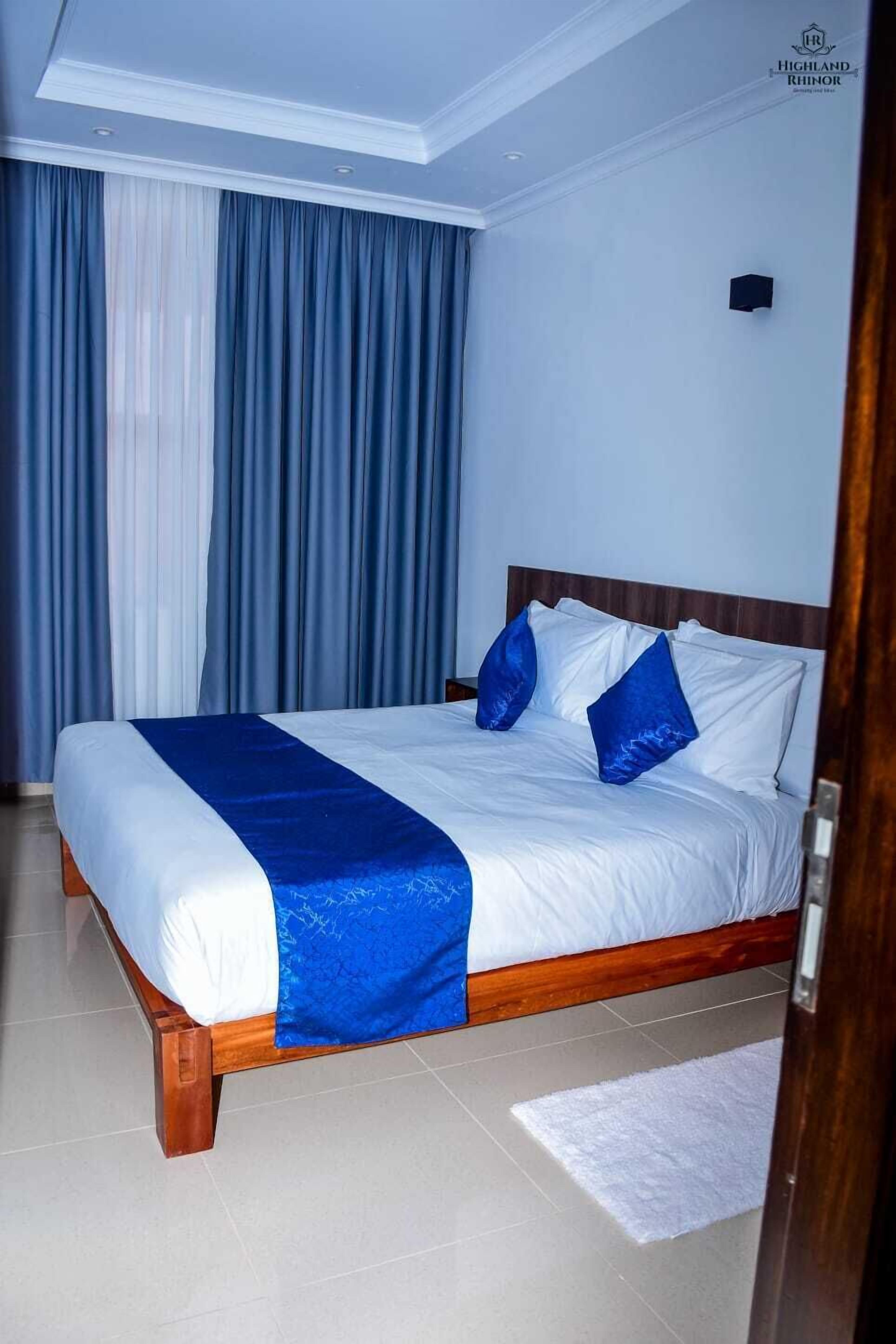A hotel room with a large bed, a wooden headboard, and a white ceiling.