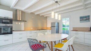 A modern kitchen with white cabinetry, stainless steel appliances, and a round dining table with chairs. - Renovated Holiday Home 'Le 36' with Private Terrace, Garden, and Wi-Fi (Jonzac)