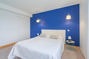 Ein Schlafzimmer mit einem Bett, zwei Wandlampen, einem runden Beistelltisch und einer Tür.