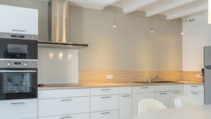 A modern kitchen with built-in appliances, a wooden countertop, and a dining area with chairs. - Renovated Holiday Home 'Le 36' with Private Terrace, Garden, and Wi-Fi (Jonzac)