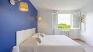 A bedroom with a bed, two wall-mounted lamps, a window with a view, and a radiator. - Renovated Holiday Home 'Le 36' with Private Terrace, Garden, and Wi-Fi (Jonzac)