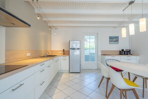 Eine moderne Küche mit weißen Schränken, einem Edelstahl-Kühlschrank und einem Essbereich mit weißem Tisch und Stühlen.