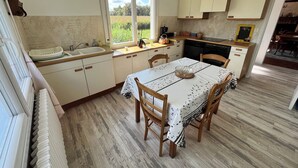 Une cuisine avec une table à manger, des chaises en bois, une fenêtre donnant sur un paysage verdoyant et des armoires blanches.