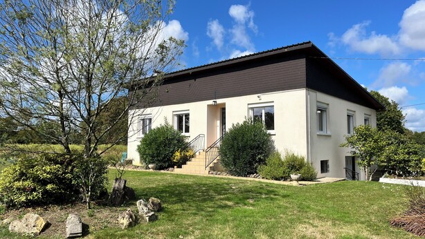 Une maison à deux étages, avec un toit sombre, des murs blancs et une entrée principale surmontée d’un escalier.