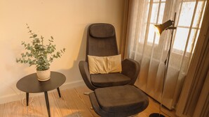Una stanza moderna con una poltrona imbottita grigia, un tavolino rotondo con una pianta in vaso e una lampada da terra.