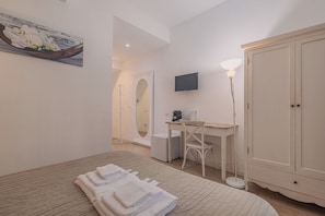 A hotel room with a bed, a desk, a television, a wardrobe, and a painting on the wall.