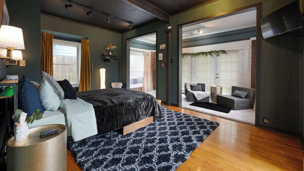 A modern bedroom with a large bed, a small side table, and a view into an adjacent living area. - Retreat on Bardstown Road | Yard • Great Location (Louisville)