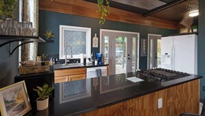 A modern kitchen with a black countertop, wooden cabinets, and a gas stove. There are potted plants and a framed picture on the counter. - Retreat on Bardstown Road | Yard • Great Location (Louisville)