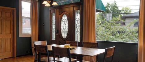 Un comedor con una mesa y sillas de madera, una ventana con un diseño decorativo y vistas a zonas verdes.