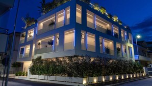 Un immeuble moderne à plusieurs étages, doté de balcons, de fenêtres illuminées et d’un jardin bien entretenu.