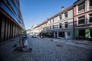 A cobblestone street lined with buildings, a parked scooter, and a car.