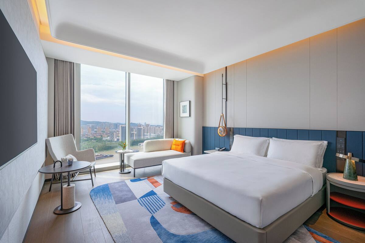 Una habitación de hotel moderna con una cama grande, un sofá, una mesita y vistas a la ciudad.