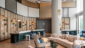 Um hall de hotel moderno com uma recepção em arco, área de estar e um espelho grande que reflete o ambiente.