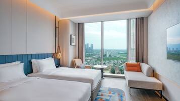 A hotel room with two beds, a sofa, a small table, and a large window offering a city view.