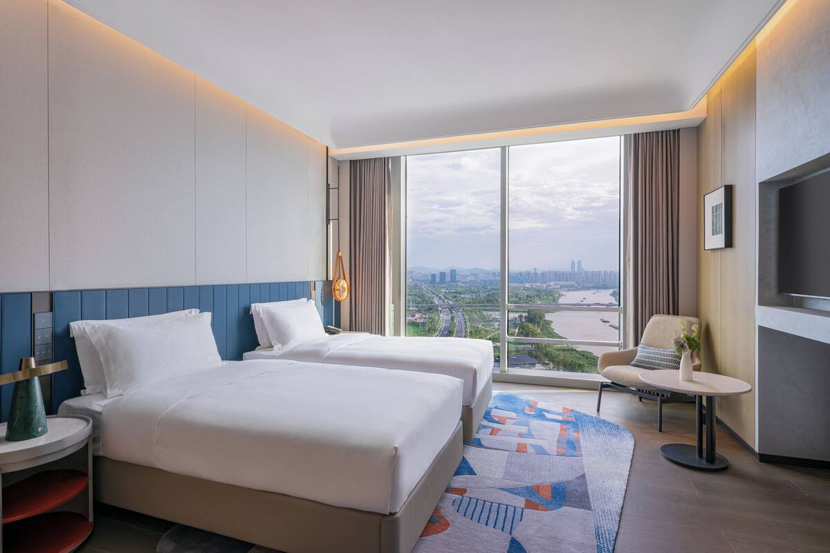 Habitación de hotel con dos camas, televisión, una mesita y vista a la ciudad.