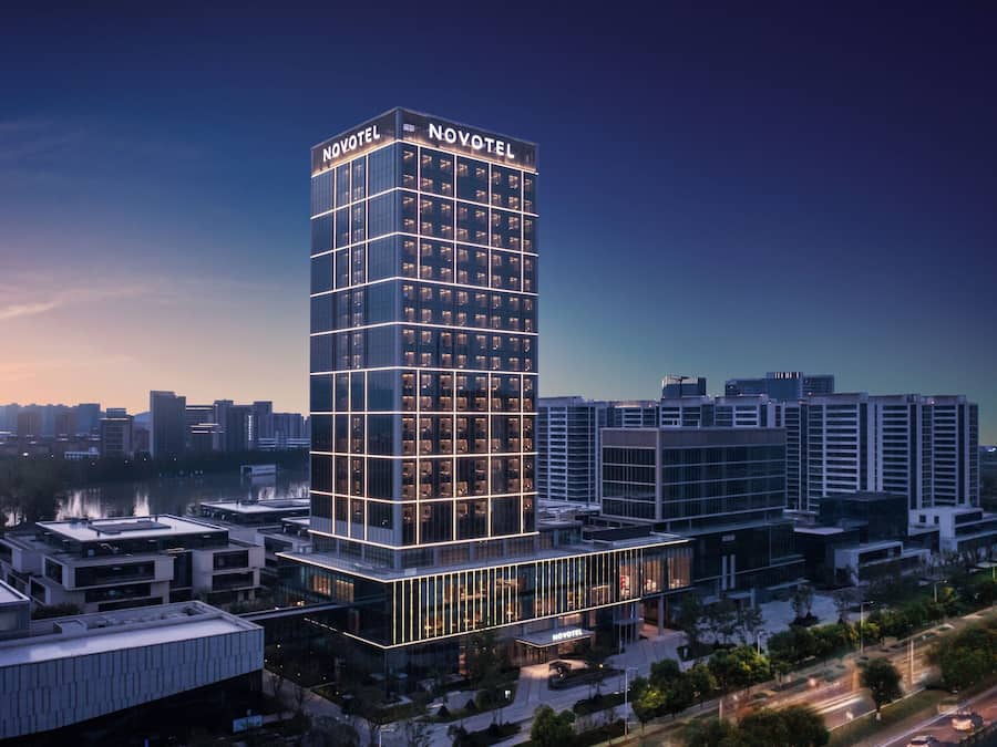 Moderni hotelli, jossa on suuri, huomiota herättävä «NOVOTEL»-kyltti, ja jonka julkisivussa on ruudukkomainen ikkunajärjestely ja lasipinta.