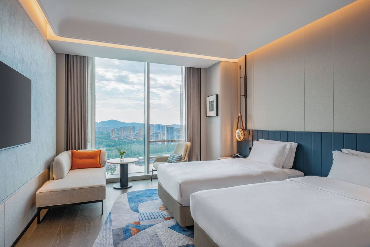 Habitación de hotel con dos camas, un sofá, una mesita y vista a la ciudad.