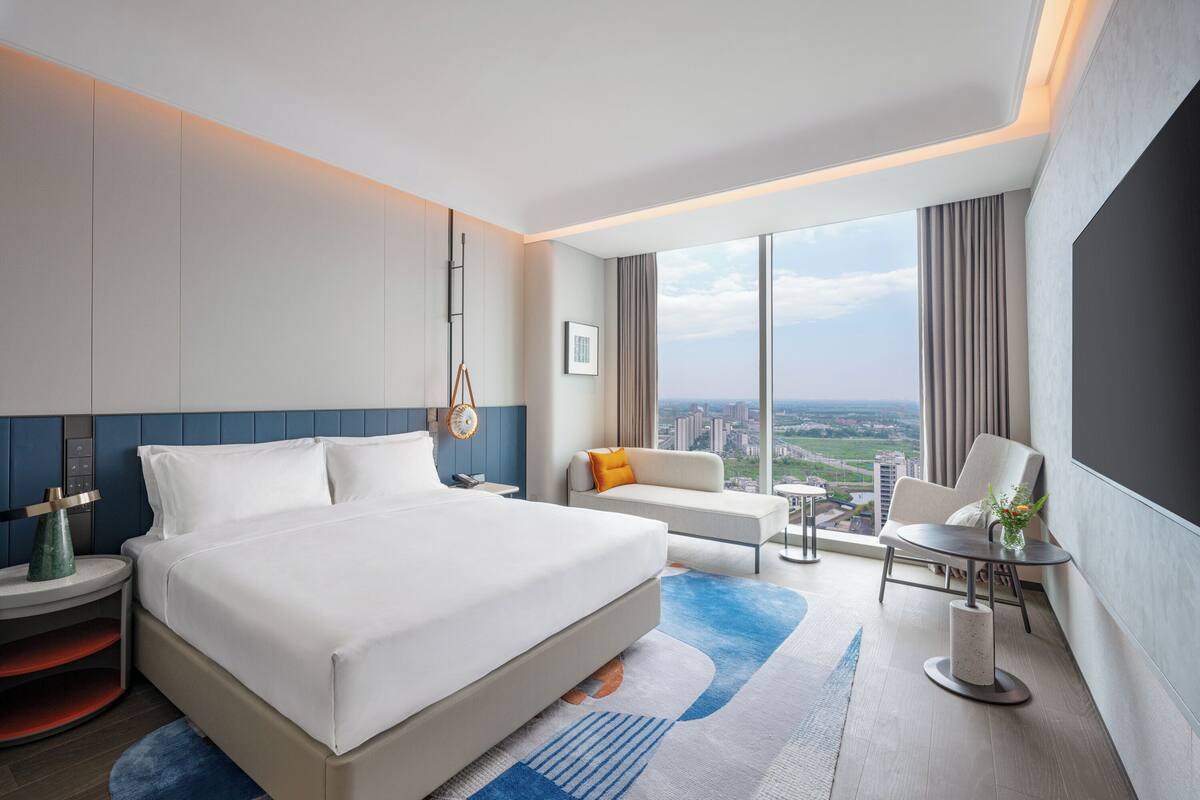 Habitación de hotel moderna con una cama grande, un sofá, una mesa de comedor y vistas a la ciudad.