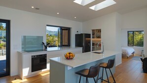 Une cuisine moderne dotée d’un îlot central, d’appareils électroménagers intégrés et de grandes fenêtres offrant une vue sur l’extérieur.