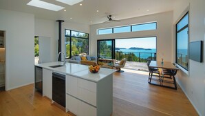 Une cuisine moderne dotée d’un îlot central, de grandes fenêtres et offrant une vue sur la mer.
