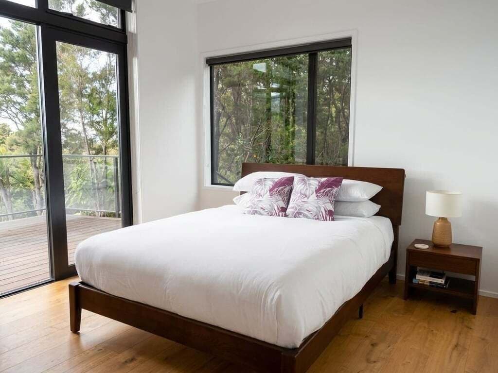A bedroom with a large window, a wooden bed, and a nightstand with a lamp.