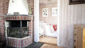 Una habitación rústica con chimenea de ladrillo, paredes de madera y una cuna con una manta roja.