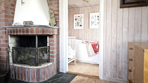 A rustic room with a brick fireplace, wooden walls, and a crib with a red blanket.