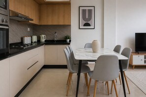 A modern kitchen with a dining area, featuring a marble table, grey chairs, and a black TV stand. - Spacieux 3 pieces a Kouba (Algiers)