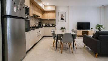 A modern kitchen with a refrigerator, stove, and microwave. There is a dining table with chairs and a sofa in the living area.