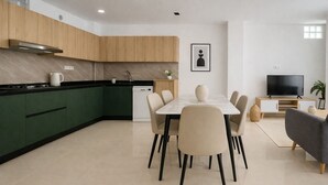A modern kitchen with green cabinets, a dining table with chairs, a TV, and a small plant. - Spacieux 3 pieces a Kouba (Algiers)