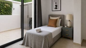 Un dormitorio moderno con cama, mesita de noche y vistas a un espacio exterior verde.