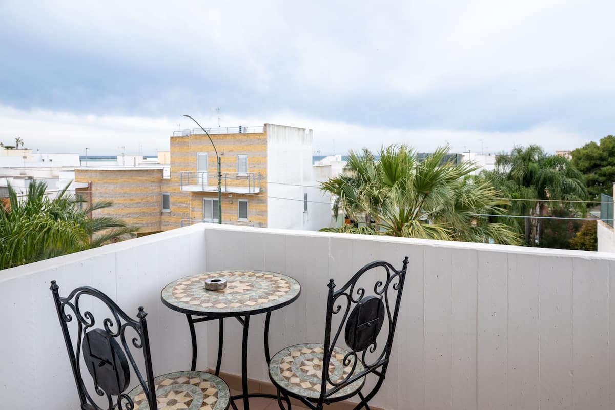 A balcony with a tiled table and two chairs, overlooking a residential area with buildings and greenery.