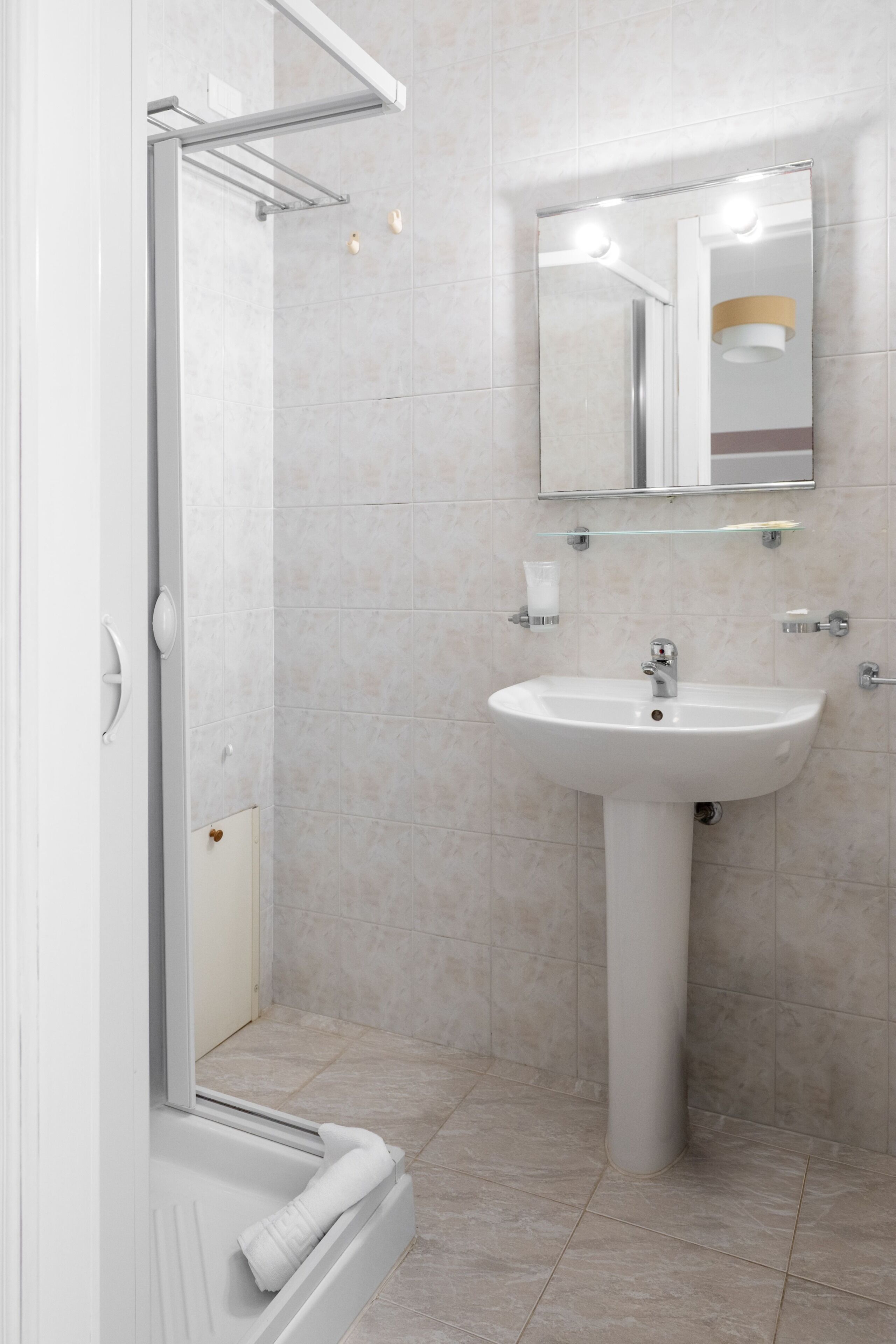 Un baño moderno con cabina de ducha de vidrio, un lavamanos pedestal y un espejo con iluminación.