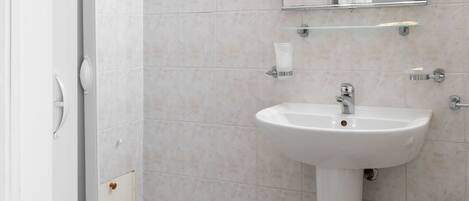 A modern bathroom with a glass shower enclosure, a pedestal sink, and a mirror with lights.