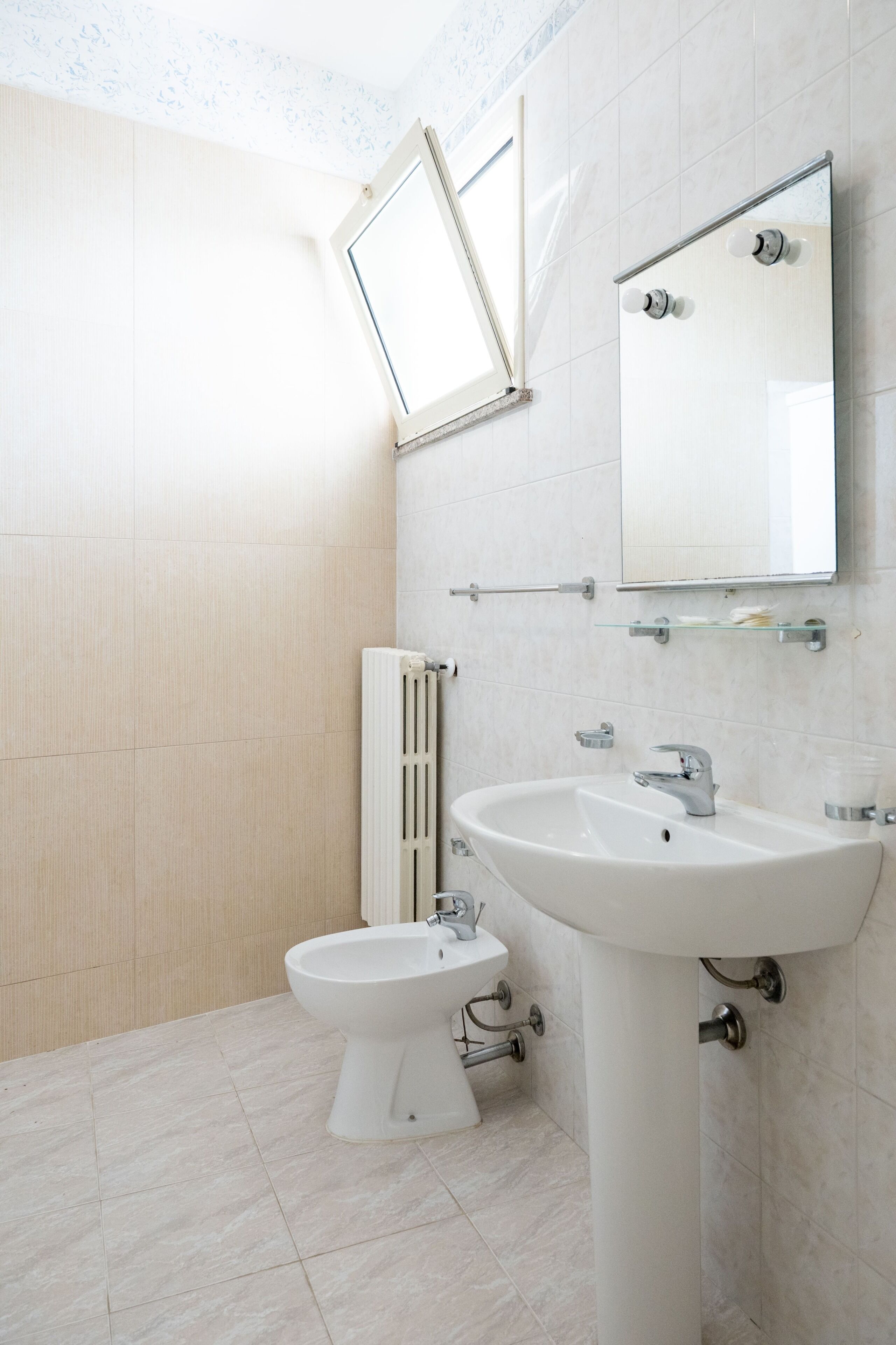 A bathroom with a pedestal sink, a mirror, a toilet, and a radiator.