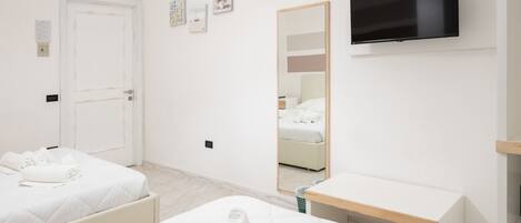 A hotel room with two beds, a desk, a TV, a mirror, and artwork on the wall.