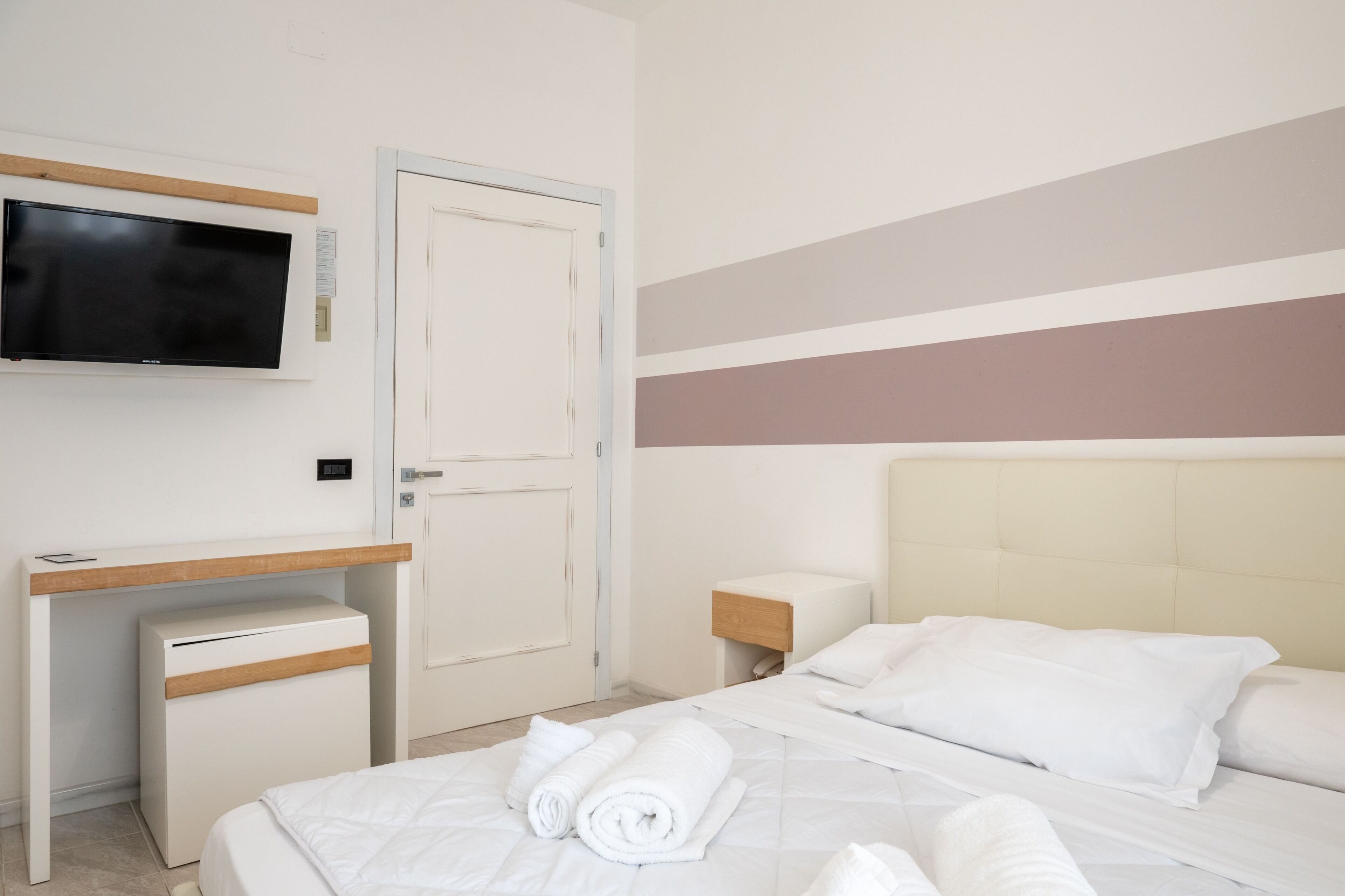 A hotel room with a bed, a desk, a television, and a door.