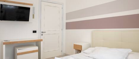 A hotel room with a bed, a desk, a television, and a door.
