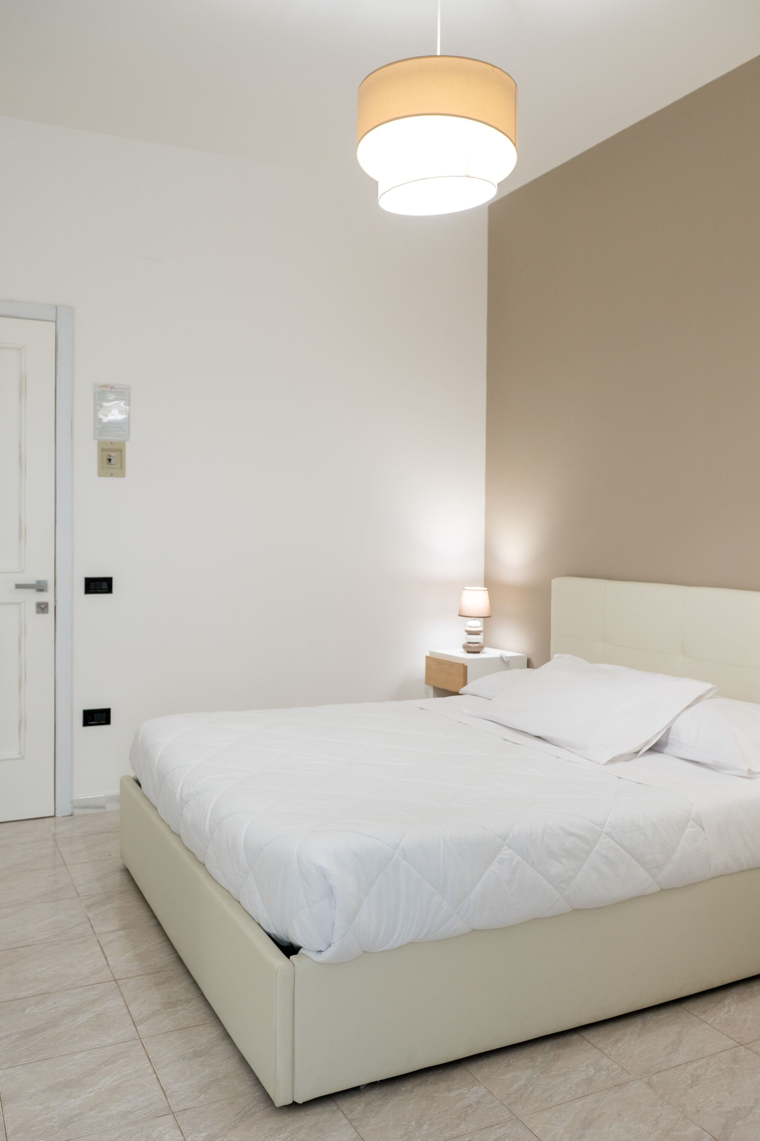 A bedroom with a bed, bedside table, lamp, and a door.